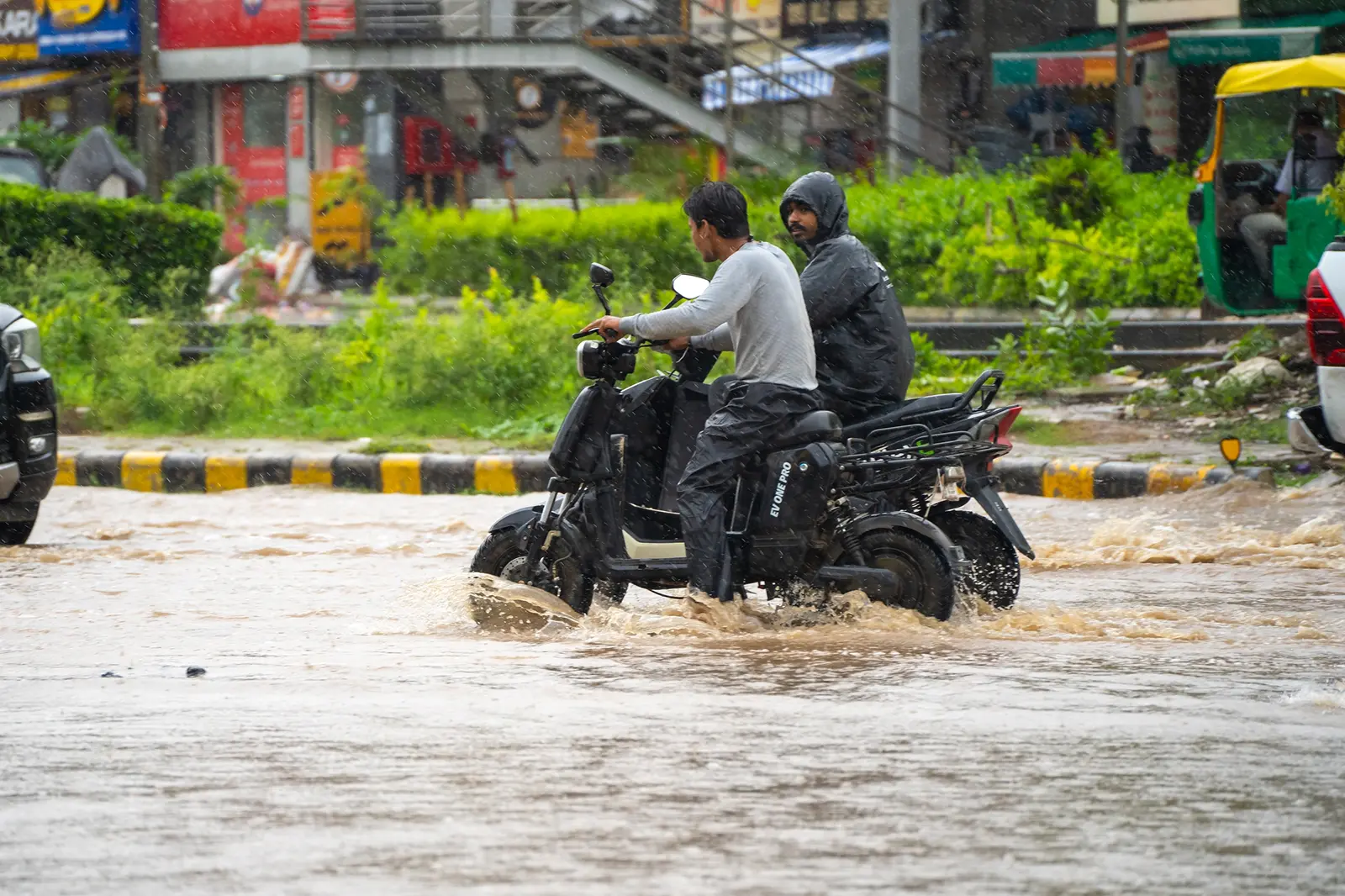 Two bikes and other vehicles on a water filled road on a heavy rain day