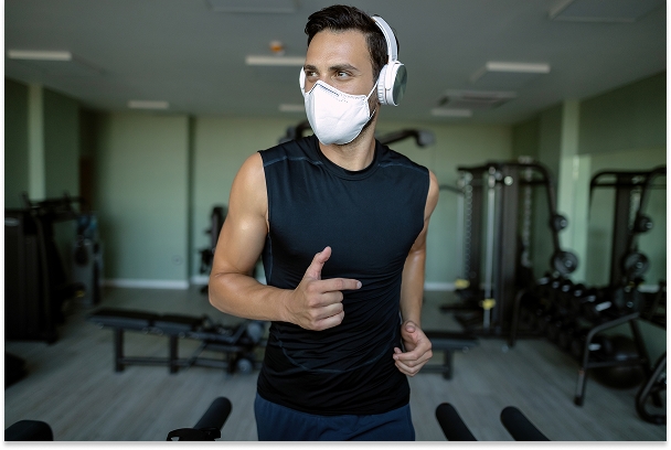 Man exercising indoors on a treadmill while wearing a face mask to protect against polluted air.